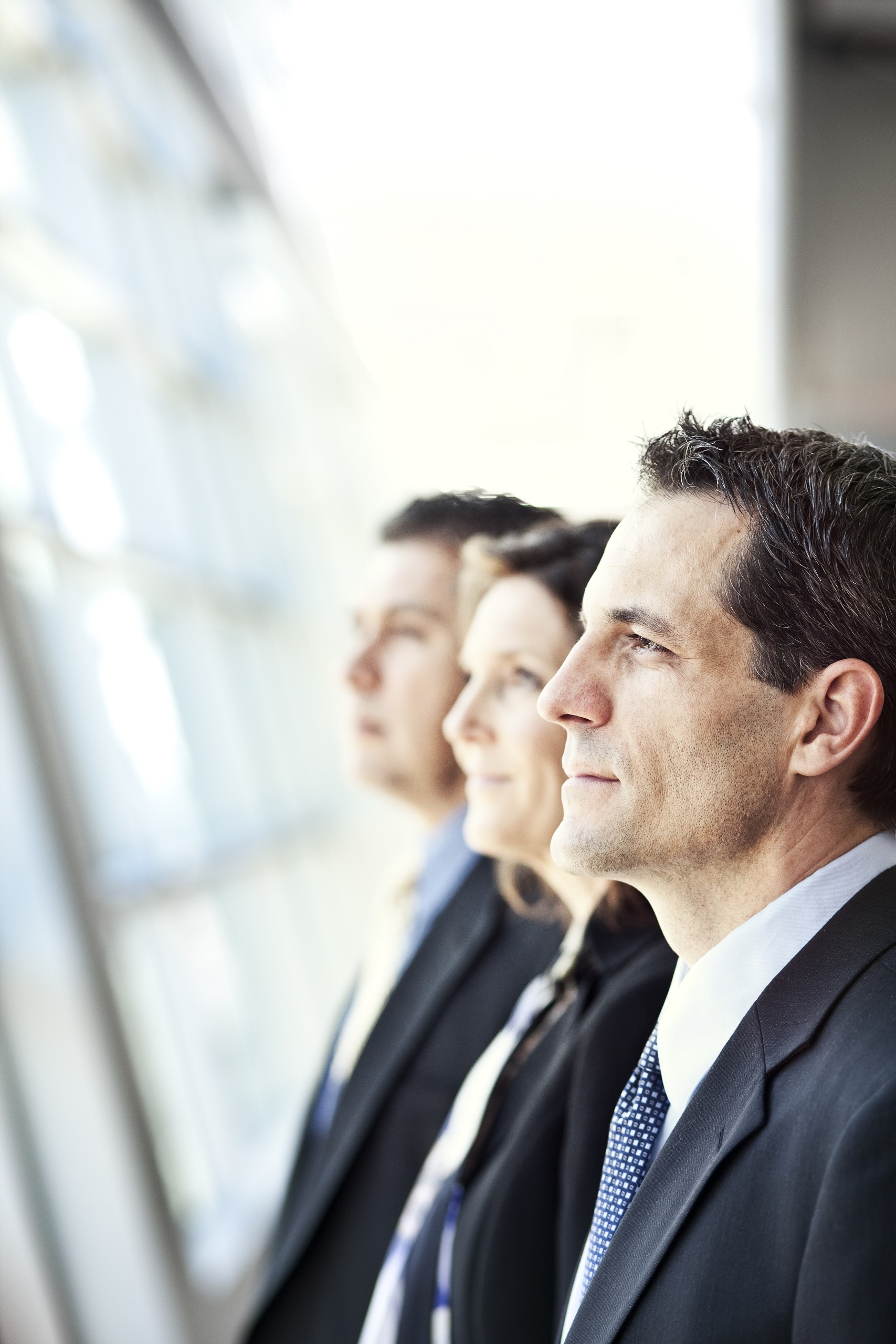 Grupo de tres personas de negocios uniformadas mirando de perfil hacia la izquierda con proposito